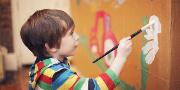 A young boy doing a large painting on a piece of card at home.