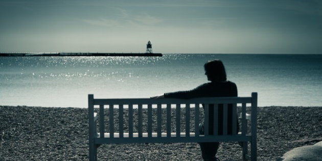 Woman in silhouette, sitting on a bench in a moody landscape at water's edge. The lone woman may be widowed, divorced, or lonely, sitting in solitude, contemplating her grief, sadness, or depression. The lighthouse in the distance is a symbol of finding hope or direction in a sea of troubles.