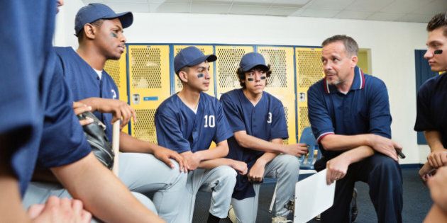 High school baseball coach talking with players in locker room