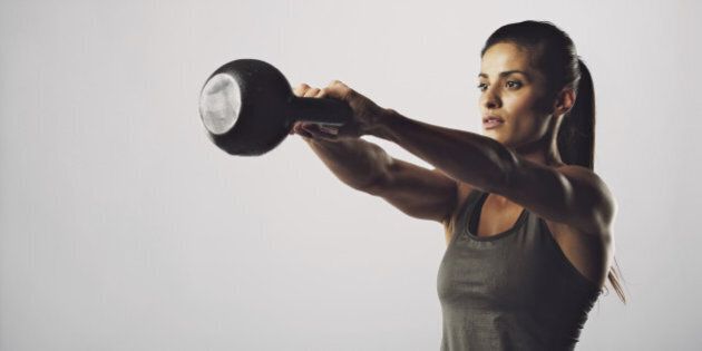 Young fitness female exercise with kettle bell. Mixed race woman doing gym workout on grey background