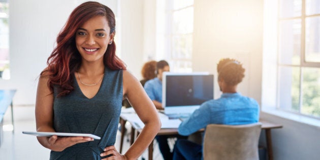 Portrait of a young entrepreneur using a digital tablet at work with her team in the background