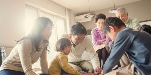 Multi-generation Family playing with wood blocks in the living room.Grandparents seen it sitting on the couch.