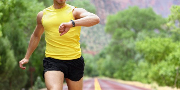 Runner with heart rate monitor sports watch. Man running looking at his pulse outside in nature on road.