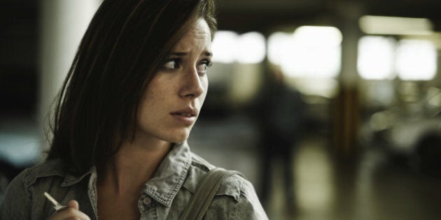 A terrified young woman in an underground parking garage being followed by a sinister man