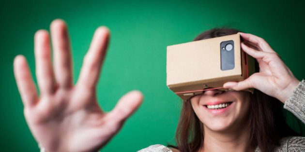 Color shot of a young woman looking through a cardboard, a device with which one can experience virtual reality on a mobile phone.