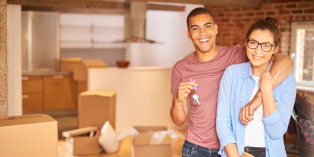 a young couple unpack their belongings as they settle into their new loft apartment . They are hugging and looking to camera smiling holding their keys aloft .