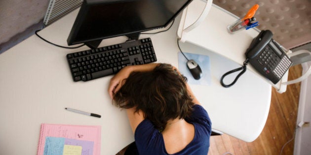 Aerial view of young woman sitting at work desk, her head is buried in her arms, office environment is modern and creative.