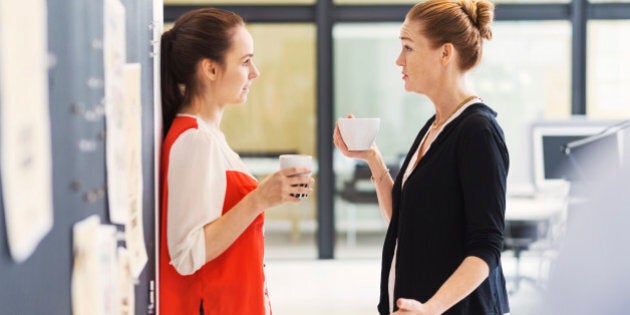 Side view of businesswomen discussing while having coffee in office