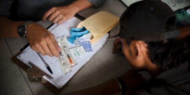 TO GO WITH AFP STORY BY JAVIER RAMIREZ FRANCOA social worker provides an addict with a sterile kit with syringes, gauze, distilled water, bandages, an elastic band and brochures with information about heroin, on February 4, 2016, in Cali, Colombia. Cali's municipal authorities through the Accion Tecnica Social (ATS) NGO chose to bet on the reduction of the damage suffered by the addicts by contagious diseases, giving them for free sterile syringes and needles. AFP PHOTO / LUIS ROBAYO / AFP / LUIS ROBAYO (Photo credit should read LUIS ROBAYO/AFP/Getty Images)