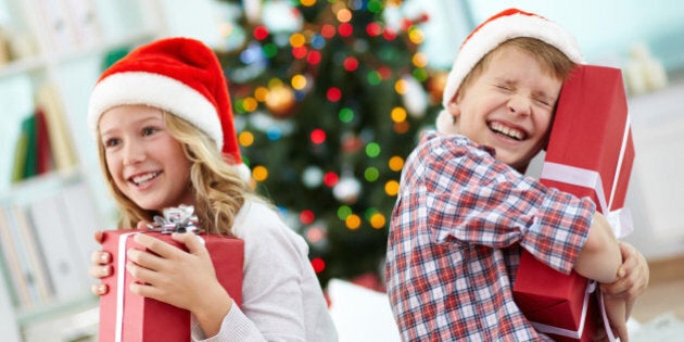 Portrait of happy siblings holding giftboxes and laughing on Christmas evening