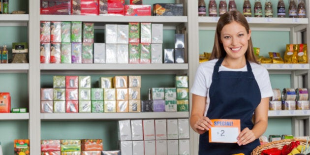 Portrait of confident saleswoman displaying pricetag in grocery store