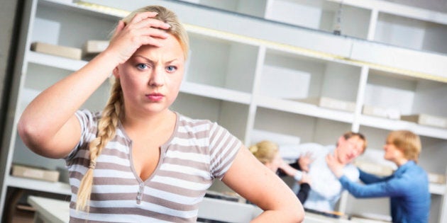 Overwhelmed female warehouse worker distraught by her team fighting behind her.