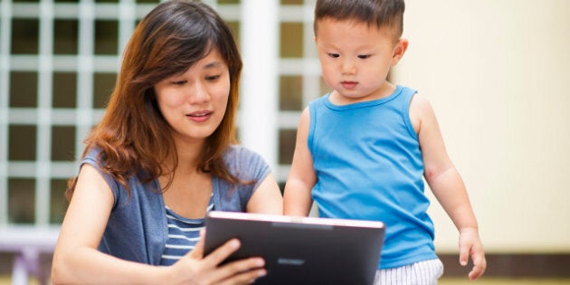 Mother and little boy looking at tablet in front of house.