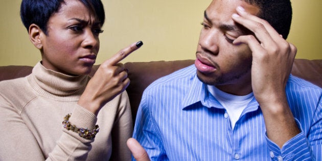 A couple is fighting on a couch and the girl is pointing her finger accusingly at him.