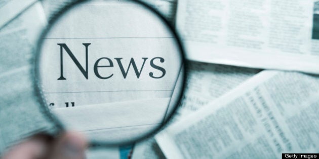 man holding a magnifying glass on the 'News' word in the stack of newspapers, blue toned image