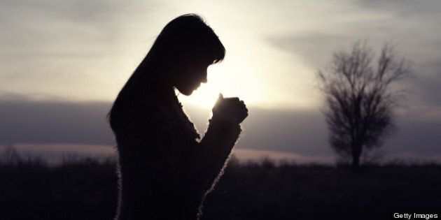 Silhouette woman praying outdoors in field with single tree.