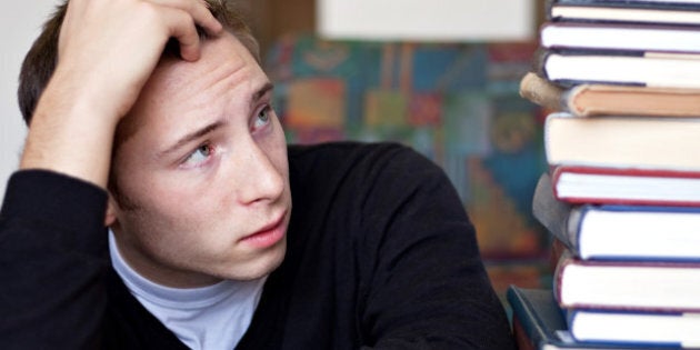 A frustrated and stressed out student looks up at the high pile of textbooks he has to go through to do his homework.