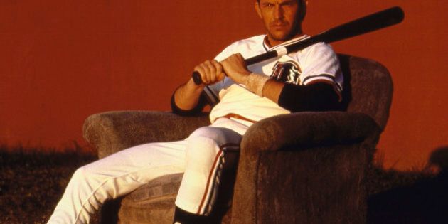 Actor Kevin Costner sitting in an upholstered chair, wearing uniform & holding a bat, during the filming of the movie Bull Durham. (Photo by Matthew Naythons//Time Life Pictures/Getty Images)