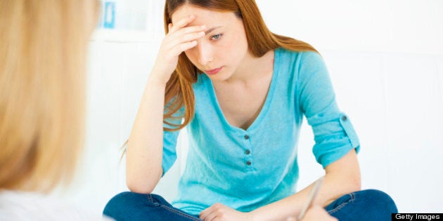 Depressed teenage girl having session with her family psychiatrist. Selective focus to her holding her head and looking down.