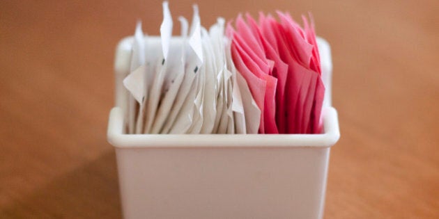 A container of sweetener and sugar packets on a table.