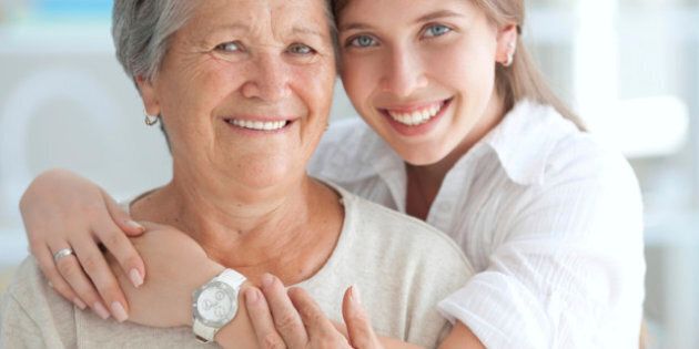 Young woman hugging her mother or grandmother and looking at camera.