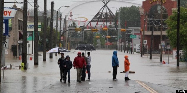 Residents stand near rising waters before the Olympic Saddledome (background) in Calgary, Alberta, Canada, June 21, 2013. Flooding forced the evacuation on Friday of some 100,000 people in the western city of Calgary and nearby towns in the heart of the Canadian oil patch. AFP PHOTO / DAVE BUSTON (Photo credit should read DAVE BUSTON/AFP/Getty Images)