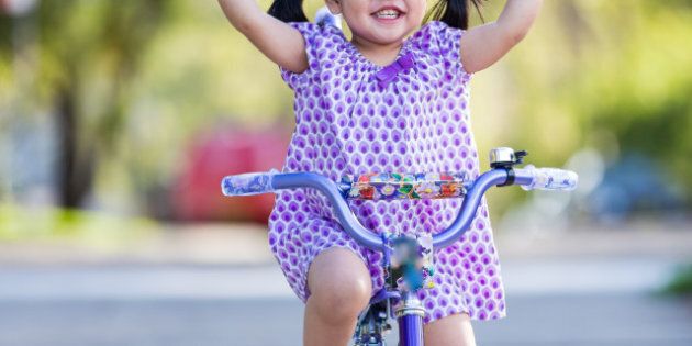 Little girl riding and smiling with her fingers held up high.