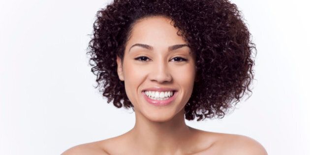 Attractive mixed race young adult woman with a beautiful face and dark brown curly hair in front of a white background smiling.