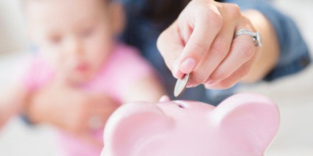 Mother with daughter (6-11 months) putting coins into piggybank