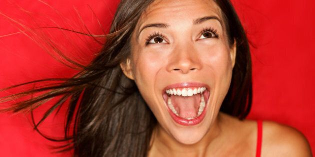 surprised screaming woman looking up at copy space on red background. Beautiful young shocked mixed race Caucasian / Asian female model amazed.