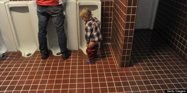 Boy pulls up pants after using the urinal in tiled restroom.