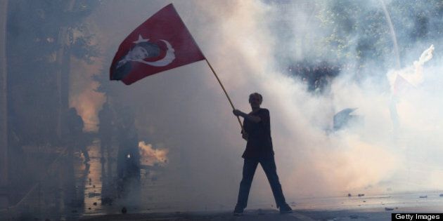 Tear gas surrounds a protestor holding a Turkish flag with a portrait of the founder of modern Turkey Mustafa Kemal Ataturk as he takes part in a demonstration in support of protests in Istanbul and against the Turkish Prime Minister and his ruling Justice and Development Party (AKP), in Ankara, on June 1, 2013. Turkish police on June 1 began pulling out of Istanbul's iconic Taksim Square, after a second day of violent clashes between protesters and police over a controversial development project. Thousands of demonstrators flooded the site as police lifted the barricades around the park and began withdrawing from the square. What started as an outcry against a local development project has snowballed into widespread anger against what critics say is the government's increasingly conservative and authoritarian agenda. AFP PHOTO / ADEM ALTAN (Photo credit should read ADEM ALTAN/AFP/Getty Images)