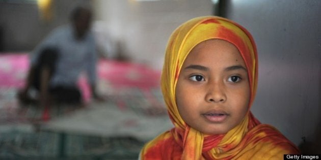 Young girl Aisha (R) watches as volunteers slaughter cattle amid prayer incantations during a religious ritual in observance of Muslim feast of Eid al-Adha outside At-Taqwa mosque in Jakarta on October 26, 2012. The meat from slaughtered cattle and goats are distributed equally to residents. Millions of Muslims around the world celebrate Eid al-Adha or 'Feast of the Sacrifice', which marks the end of the annual hajj or pilgrimage to Mecca and celebrates Abraham's readiness to sacrifice his son to God. AFP PHOTO / ROMEO GACAD (Photo credit should read ROMEO GACAD/AFP/Getty Images)