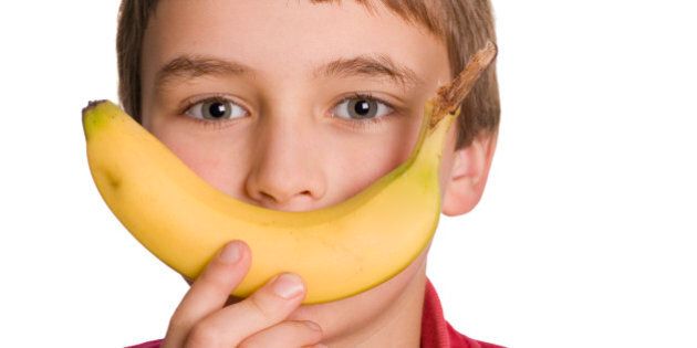 'A primary school aged boy is happy to eat a healthy banana. Isolated on a clean white background. Adobe RGB 1998 profile. Part of a larger set of images related to education, children and healthy eating.'