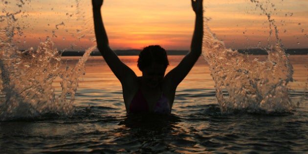 girl very splashing in the water at the beach creating many splashes over their heads against the backdrop of setting sun