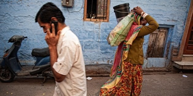 Man talking on mobile phone and woman carrying bags on her head in a typical blue street in old town. Jodhpur, Rajasthan, India