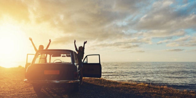 Full length shot of two friends on a road trip to the beach at sunset