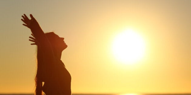 Woman breathing fresh air at sunset on the beach and raising arms