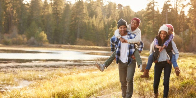 Parents Giving Children Piggyback Ride On Walk By Lake