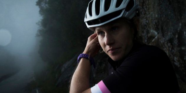 Female cyclist on mountain road, ajusting helmet