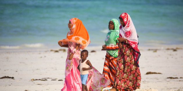 Kiwengwa Beach, Zanzibar, Tanzania - January 09, 2017: Local women with child walking along beach in traditional colorful clothes
