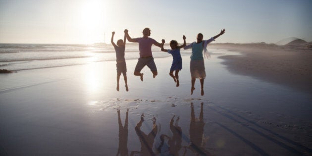 Family with two children jumping together on a beach at sunset