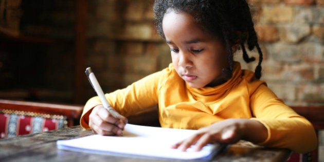 Profile of little African girl writing at home.