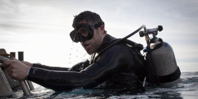 A male scuba diver takes his first breath above water as he climbs back on board a boat