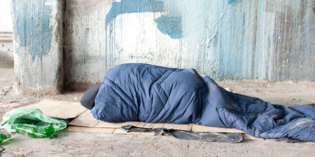 Homeless man sleeping in sleeping bag on cardboard