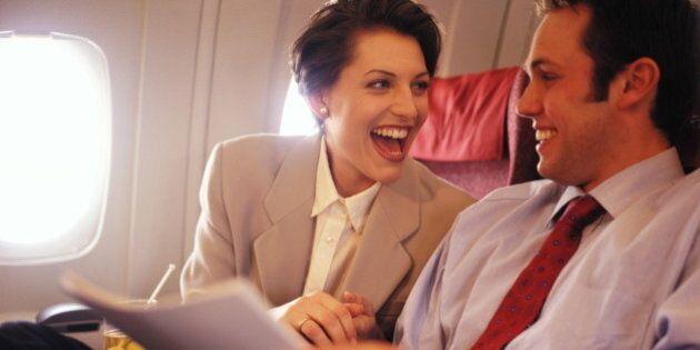 Two executives sitting in passenger aircraft, laughing and smiling