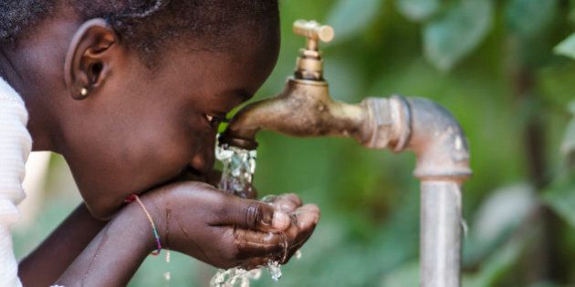 Young African girl drinking clean water from a tap. Hands cupped of an African child with water pouring from a tap in the streets of the African city Bamako, Mali.