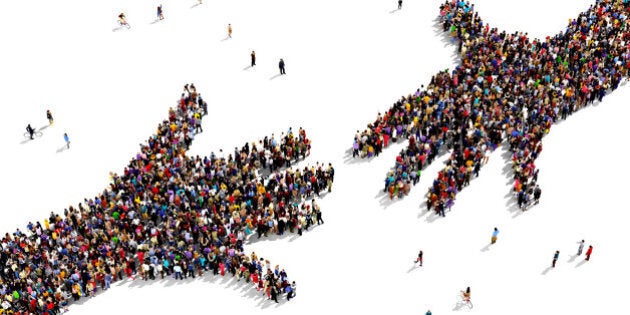 Large group of people seen from above gathered together in the shape of two hands reaching out each other