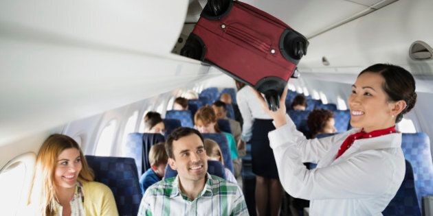 Flight attendant putting luggage in overhead bin in airplane