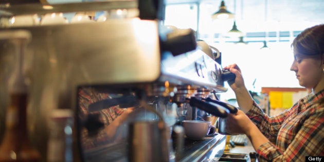 A person, barista making coffee, and frothing milk using a steam pipe, for a cappuccino. Coffee shop.